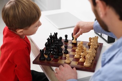Father and son playing chess at table indoors, closeup