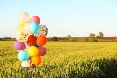 Photo of Young woman with colorful balloons in field on sunny day