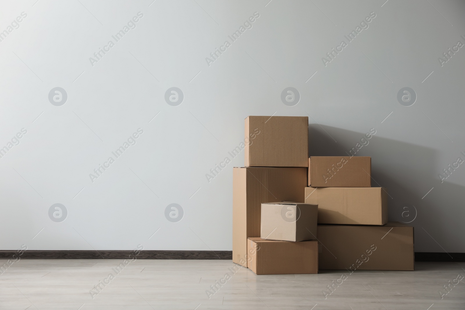 Photo of Many closed cardboard boxes on floor near white wall, space for text. Delivery service