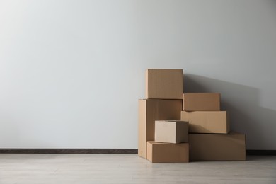 Photo of Many closed cardboard boxes on floor near white wall, space for text. Delivery service