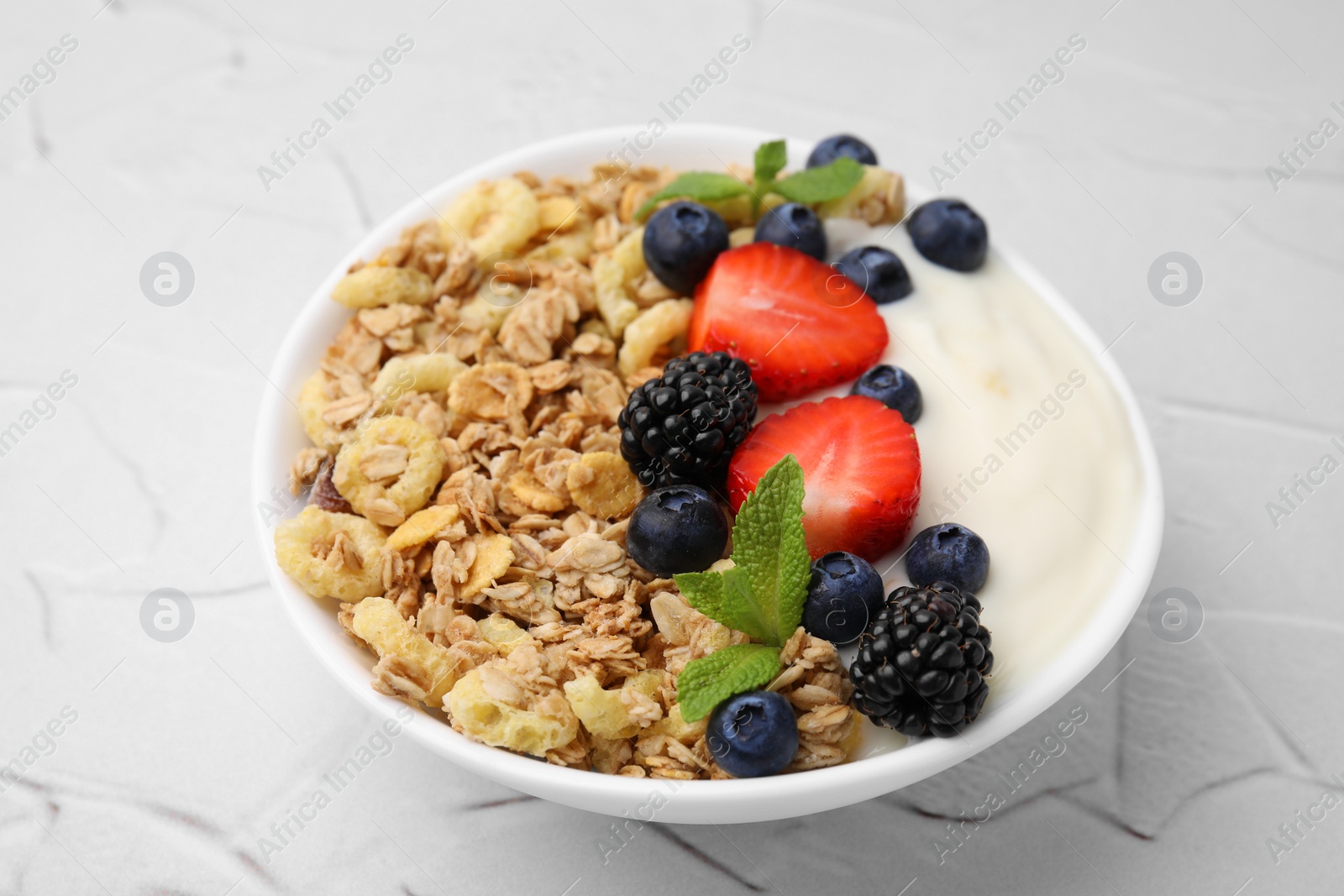 Photo of Tasty oatmeal, yogurt and fresh berries in bowl on white textured table, closeup. Healthy breakfast