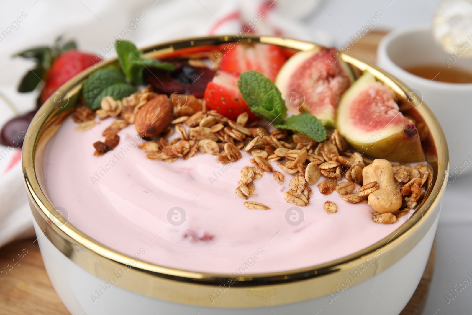 Photo of Bowl with yogurt, fruits and granola on white table, closeup