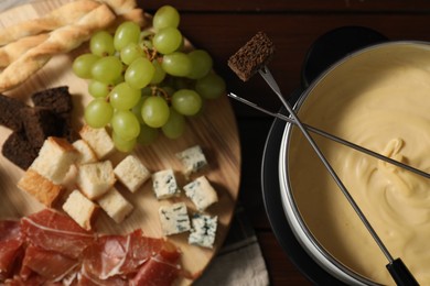 Photo of Fondue with tasty melted cheese, forks and different snacks on wooden table, top view