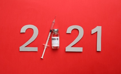 Photo of Paper numbers, syringe and vial with coronavirus vaccine forming 2021 on red background, flat lay