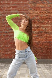 Photo of Portrait of beautiful young woman near brick wall outdoors. Hip hop dancer