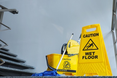 Safety sign with phrase Caution wet floor and mop bucket, indoors. Cleaning service