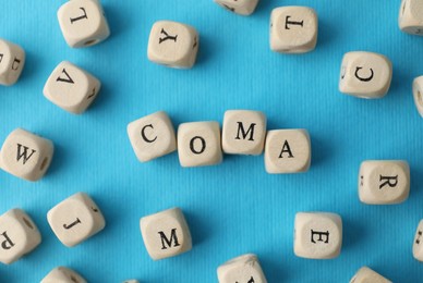 Photo of Wooden cubes with word Coma among others on light blue background, flat lay