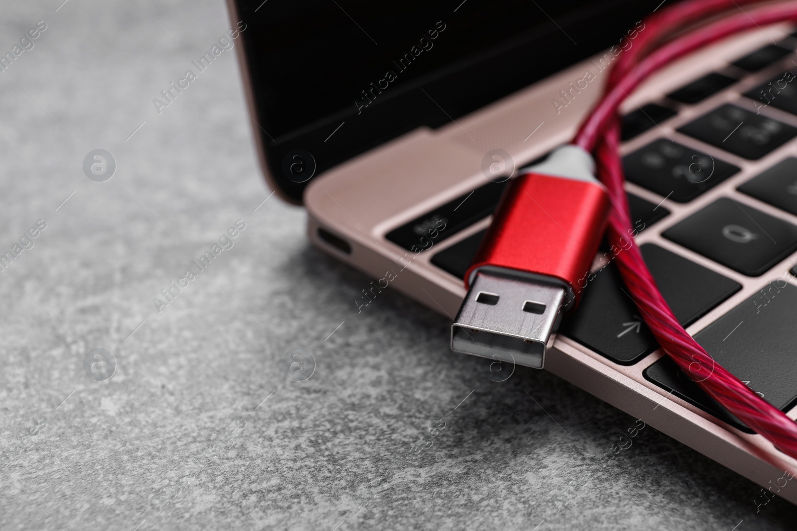 Photo of Red USB cable and laptop on grey table, closeup. Space for text