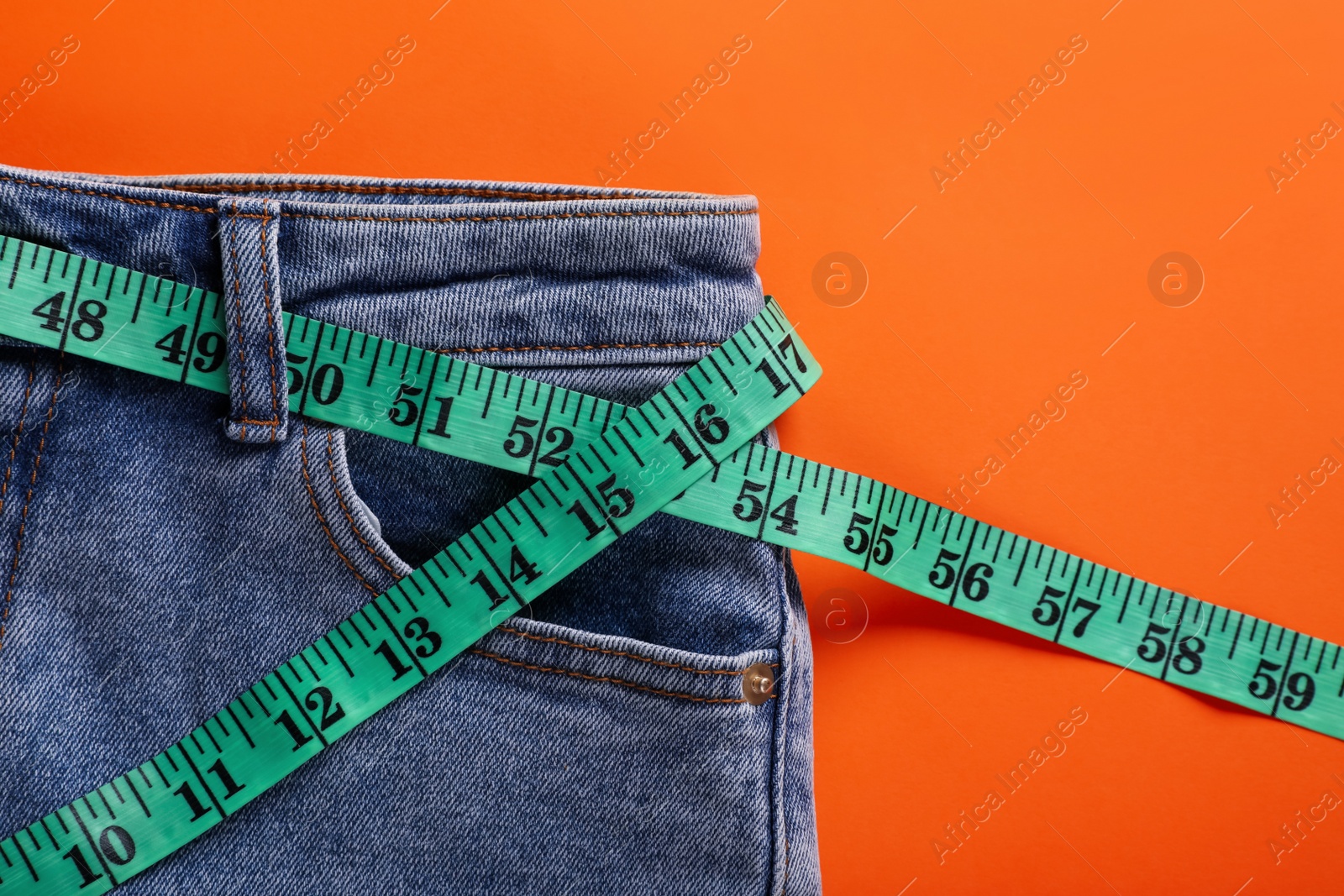 Photo of Jeans and measuring tape on orange background, top view. Weight loss concept