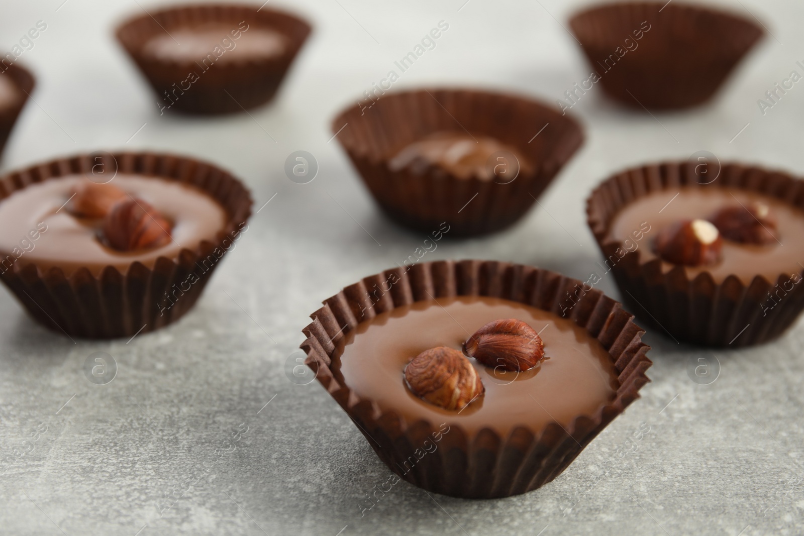 Photo of Delicious chocolate candies with hazelnuts on grey table, closeup