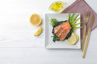 Photo of Tasty salmon with spinach served on white wooden table, flat lay