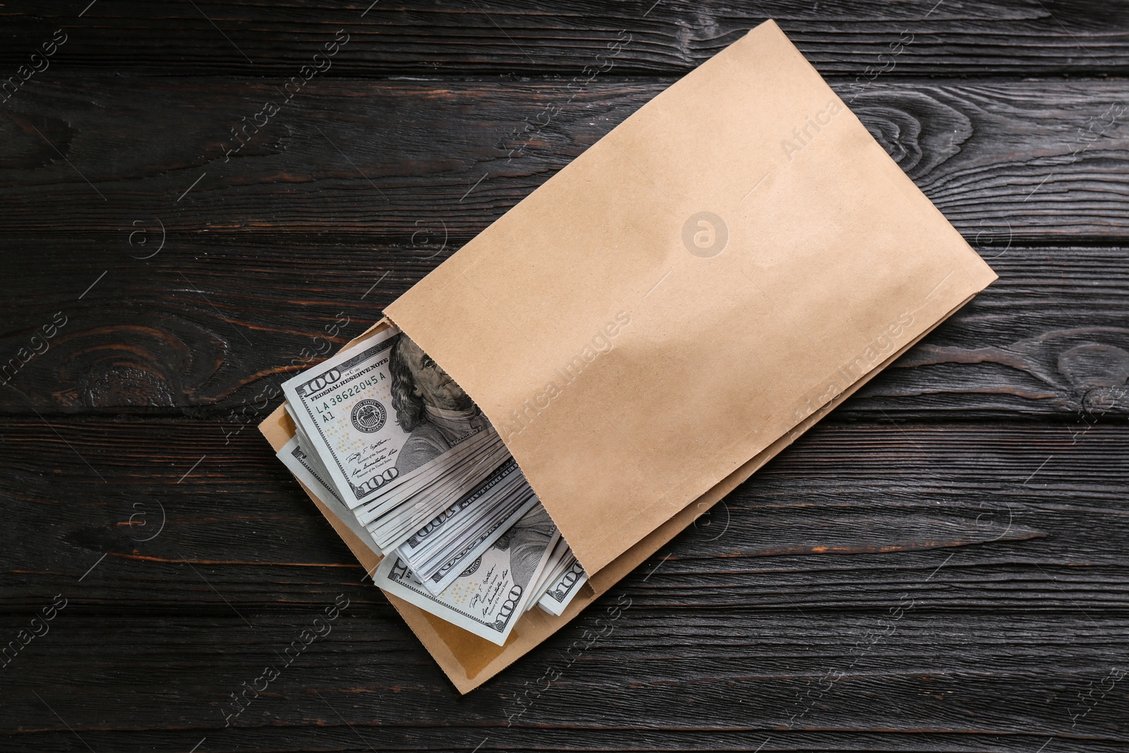 Photo of Envelope with dollar bills on black wooden table, top view. Bribe concept