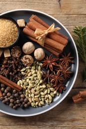 Plate with different aromatic spices on wooden table, top view