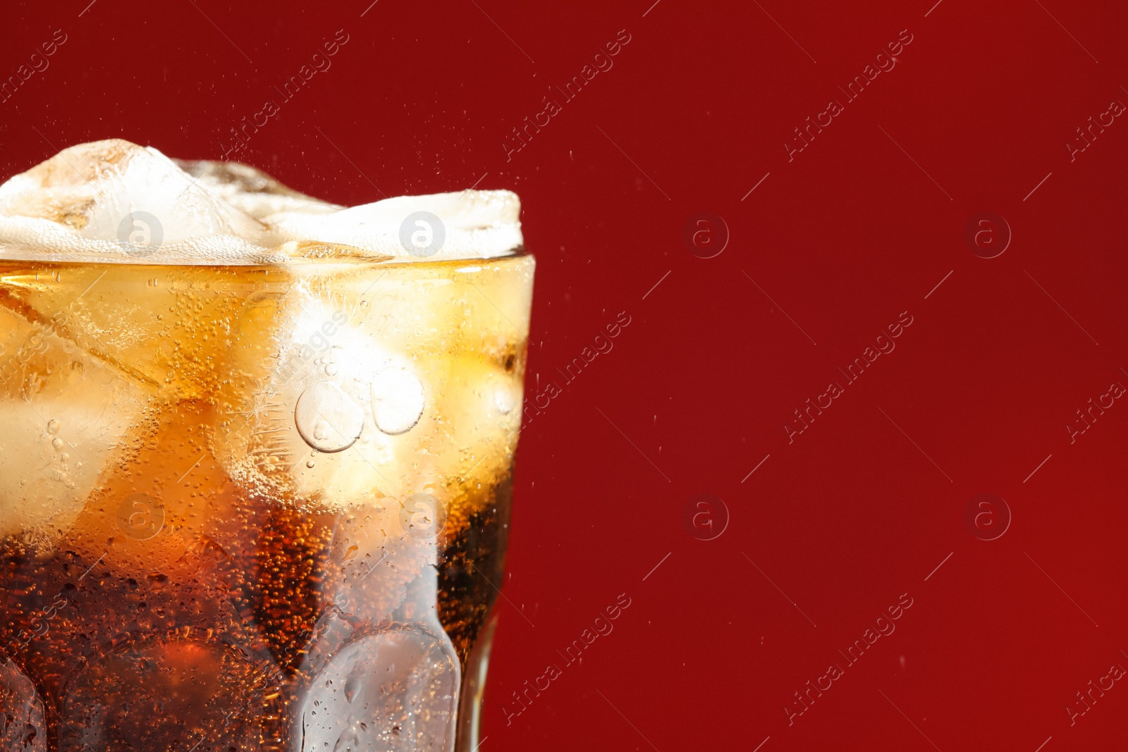 Photo of Glass of refreshing soda drink with ice cubes on red background, closeup. Space for text