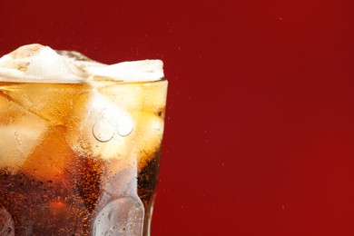Glass of refreshing soda drink with ice cubes on red background, closeup. Space for text