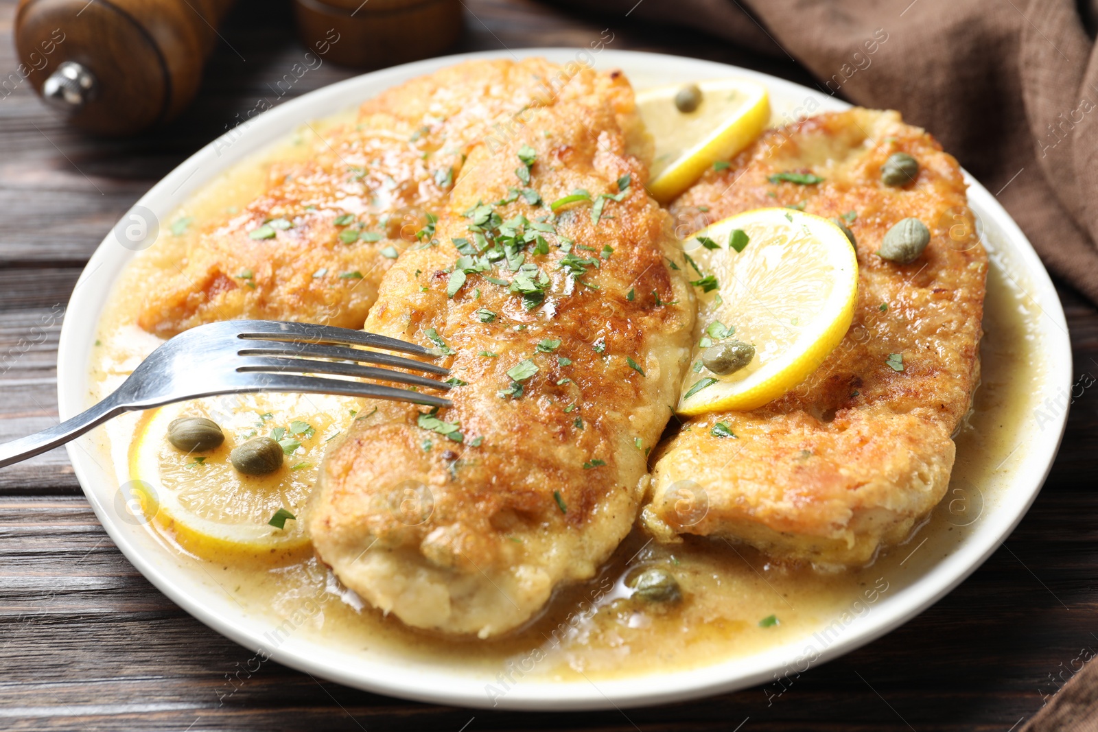 Photo of Delicious chicken piccata on wooden table, closeup