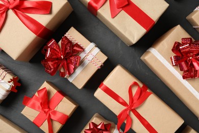 Photo of Christmas gift boxes with red bows on dark grey background, flat lay