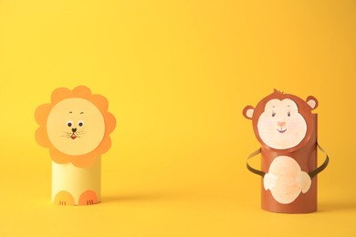 Photo of Toy monkey and lion made from toilet paper hubs on yellow background, space for text. Children's handmade ideas