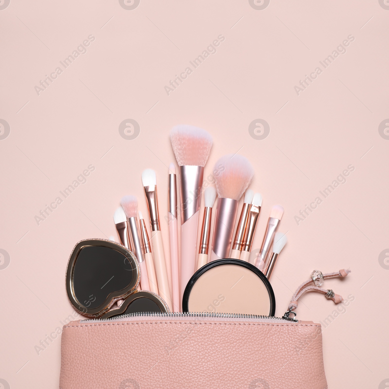 Photo of Makeup brushes, powder and mirror in cosmetic bag on pink background, flat lay