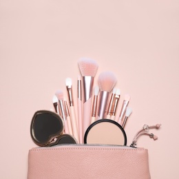 Makeup brushes, powder and mirror in cosmetic bag on pink background, flat lay