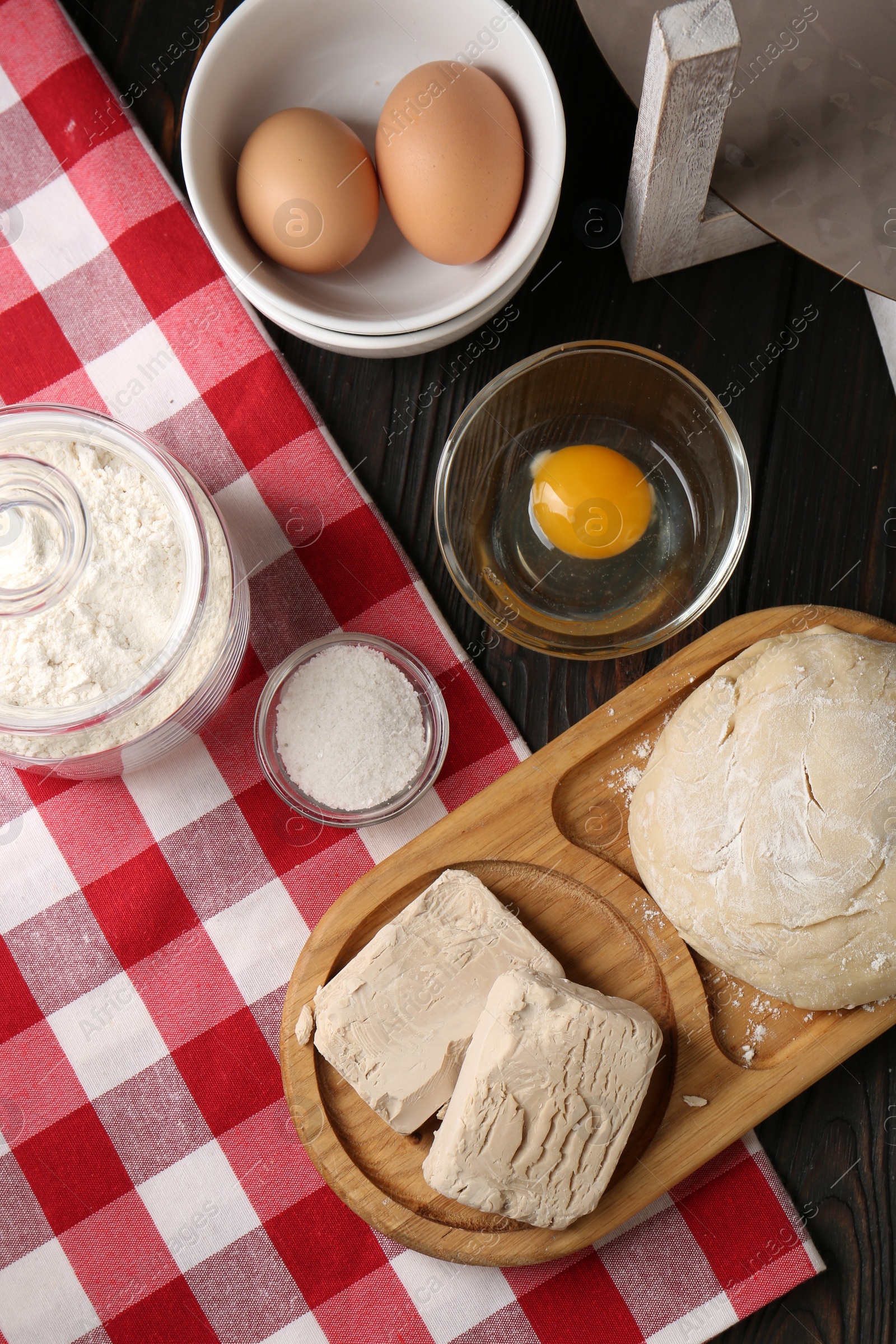 Photo of Compressed yeast, salt, flour, eggs and dough on wooden table, flat lay