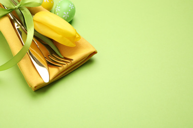 Photo of Closeup view of cutlery set with floral decor on green background, space for text. Easter celebration