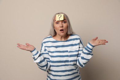 Photo of Emotional mature woman with question mark on beige background