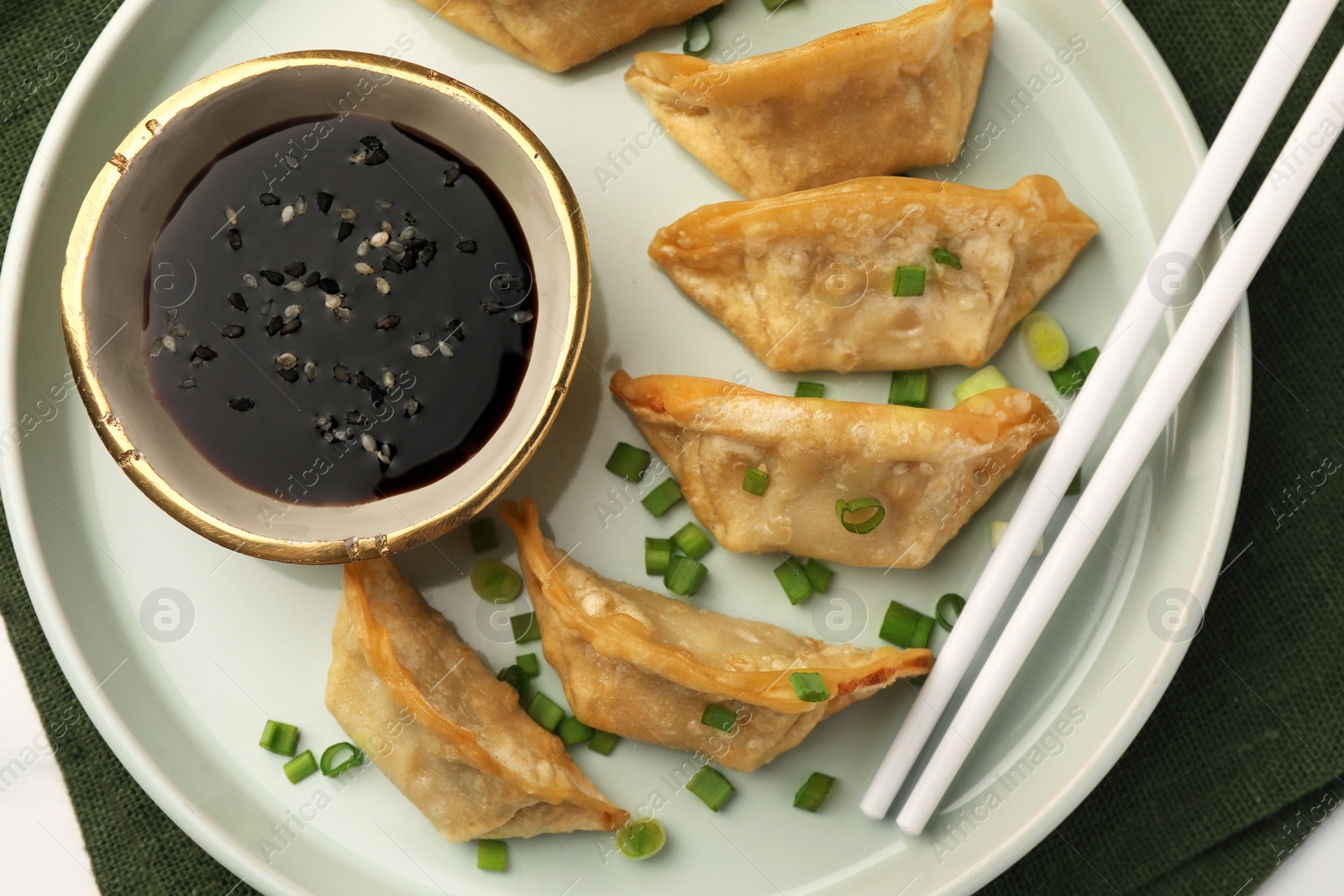 Photo of Delicious gyoza (asian dumplings) with soy sauce, green onions and chopsticks on table, top view