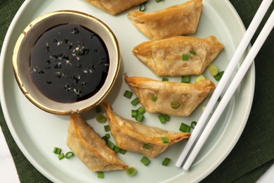 Photo of Delicious gyoza (asian dumplings) with soy sauce, green onions and chopsticks on table, top view