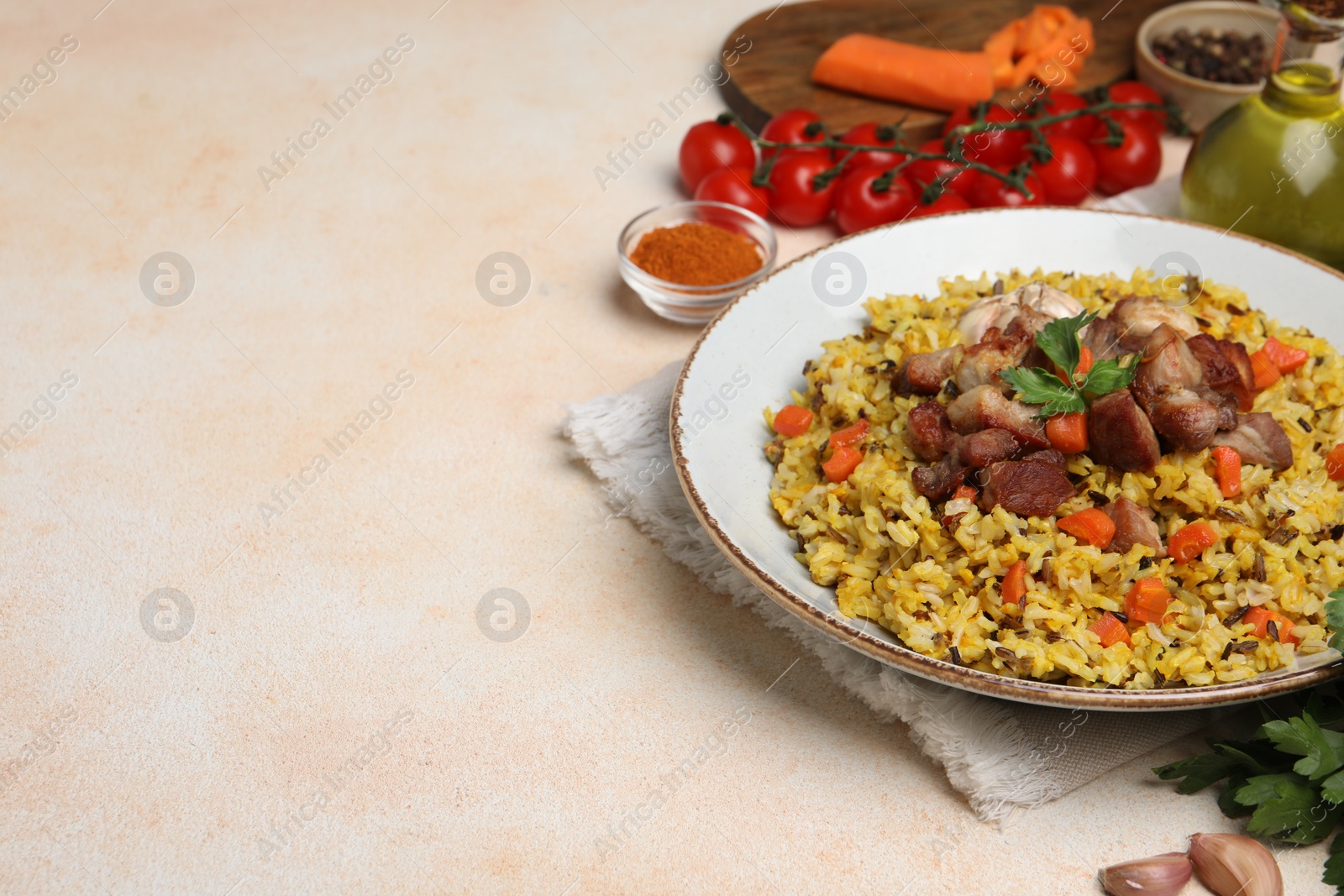 Photo of Delicious pilaf with meat, carrot and garlic on beige textured table. Space for text