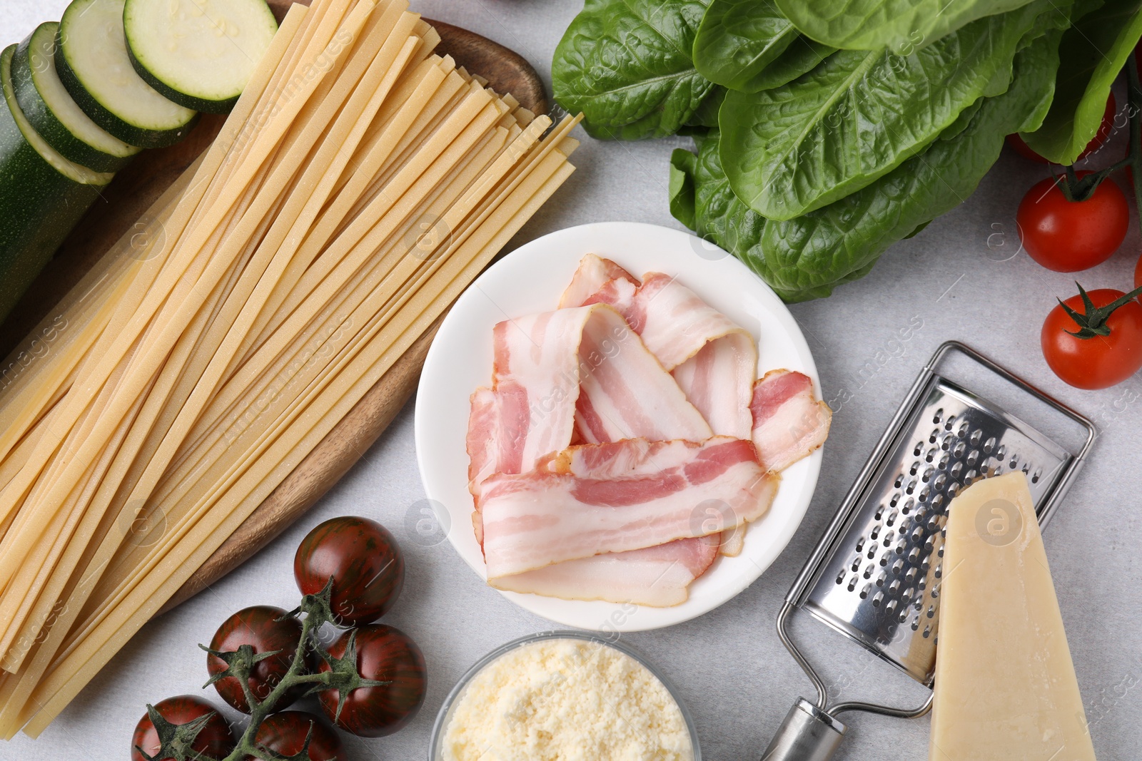 Photo of Raw pasta, bacon and fresh ingredients on light grey table, flat lay