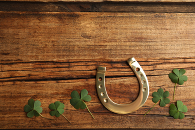 Photo of Clover leaves and horseshoe on wooden table, flat lay with space for text. St. Patrick's Day celebration