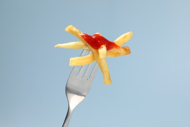 Photo of Fork with tasty french fries against light blue background, closeup