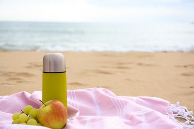 Photo of Metallic thermos with hot drink, fruits and plaid on sandy beach near sea, space for text