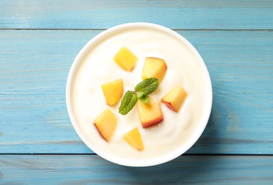 Photo of Delicious yogurt with fresh peach and mint on light blue wooden table, top view