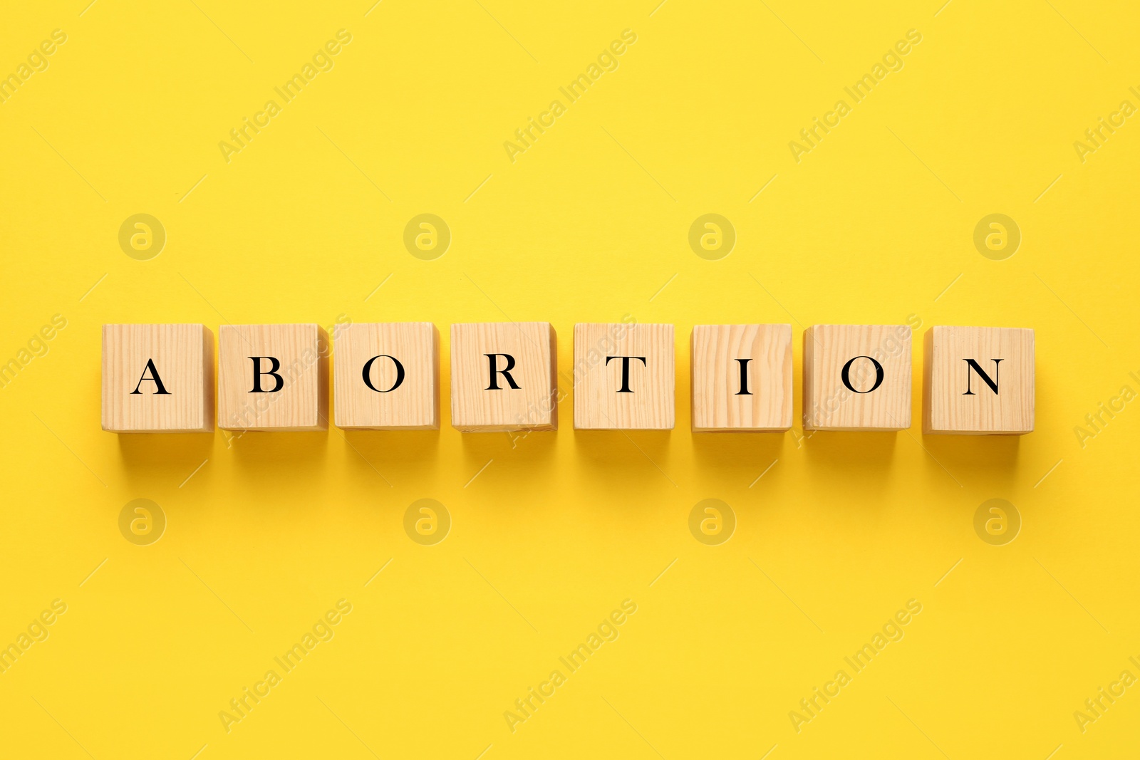 Photo of Word Abortion made of wooden cubes on yellow background, flat lay