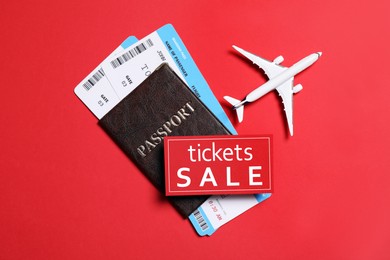 Photo of Flight tickets, passport, plane model and SALE card on red background, flat lay