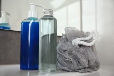 Photo of Grey shower puff and cosmetic products on washbasin in bathroom, closeup