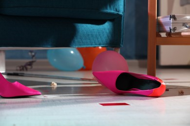 Photo of Pink shoes and playing cards on floor in messy room after party