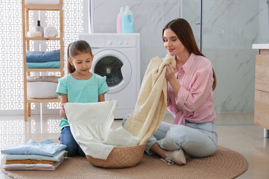 Photo of Mother and little daughter with clean laundry in bathroom