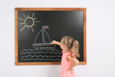 Photo of Little child drawing ship with colorful chalk on blackboard