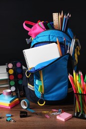Photo of Backpack with different school stationery on wooden table near blackboard