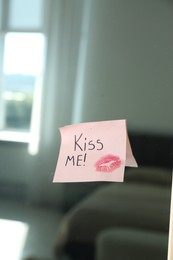 Photo of Sticky note with phrase Kiss Me and lipstick mark attached to mirror in room