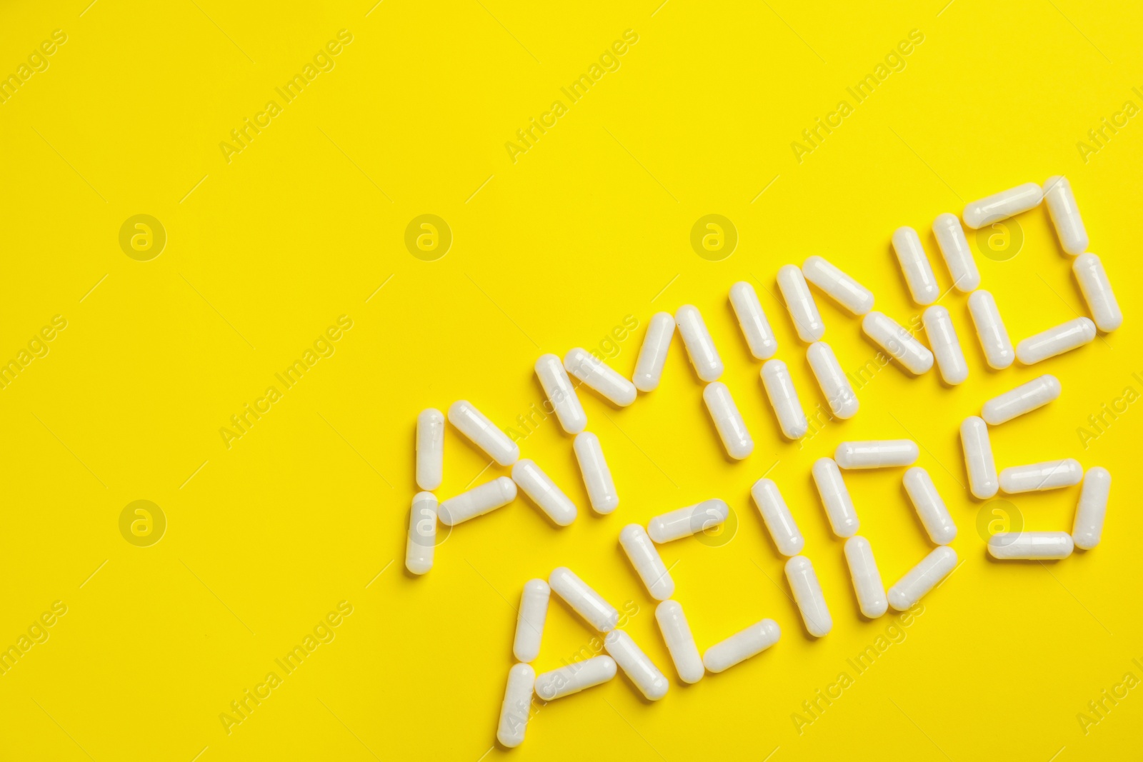 Photo of Phrase Amino acids made of pills on yellow background, flat lay. Space for text