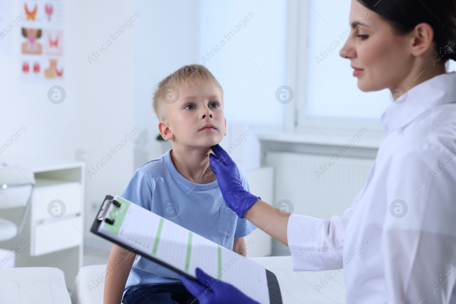 Photo of Endocrinologist with clipboard examining boy's thyroid gland at hospital