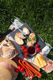 Photo of Blanket with wine and snacks for picnic on green grass, flat lay