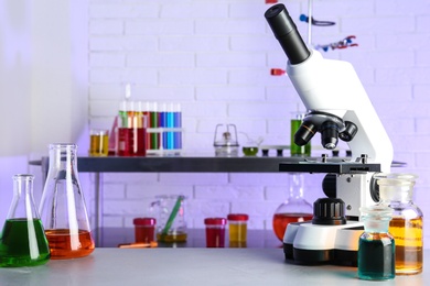 Photo of Different glassware with samples and microscope on table in chemistry laboratory. Space for text