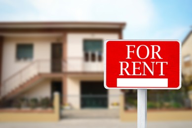Image of Sign with phrase FOR RENT and blurred view of beautiful house