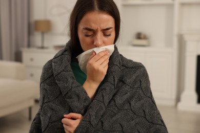 Photo of Sick woman wrapped in blanket with tissue blowing nose at home. Cold symptoms