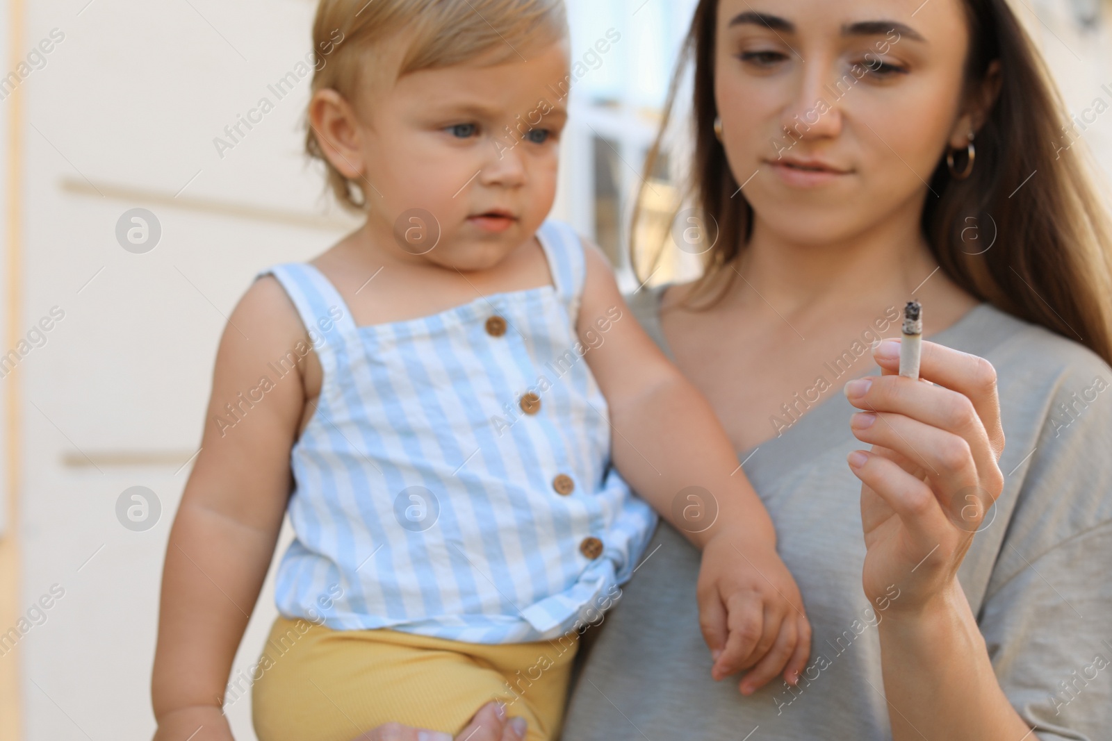 Photo of Mother with cigarette and child outdoors, focus on hand. Don't smoke near kids